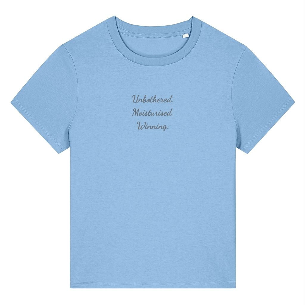 Light blue organic cotton women's t-shirt featuring the confidence quote ‘Unbothered. Moisturised. Winning.’ by Rivaex Clothing